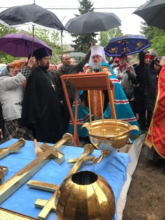 Прихожане с зонтами наблюдают за освящением куполов у ограды строящегося храма